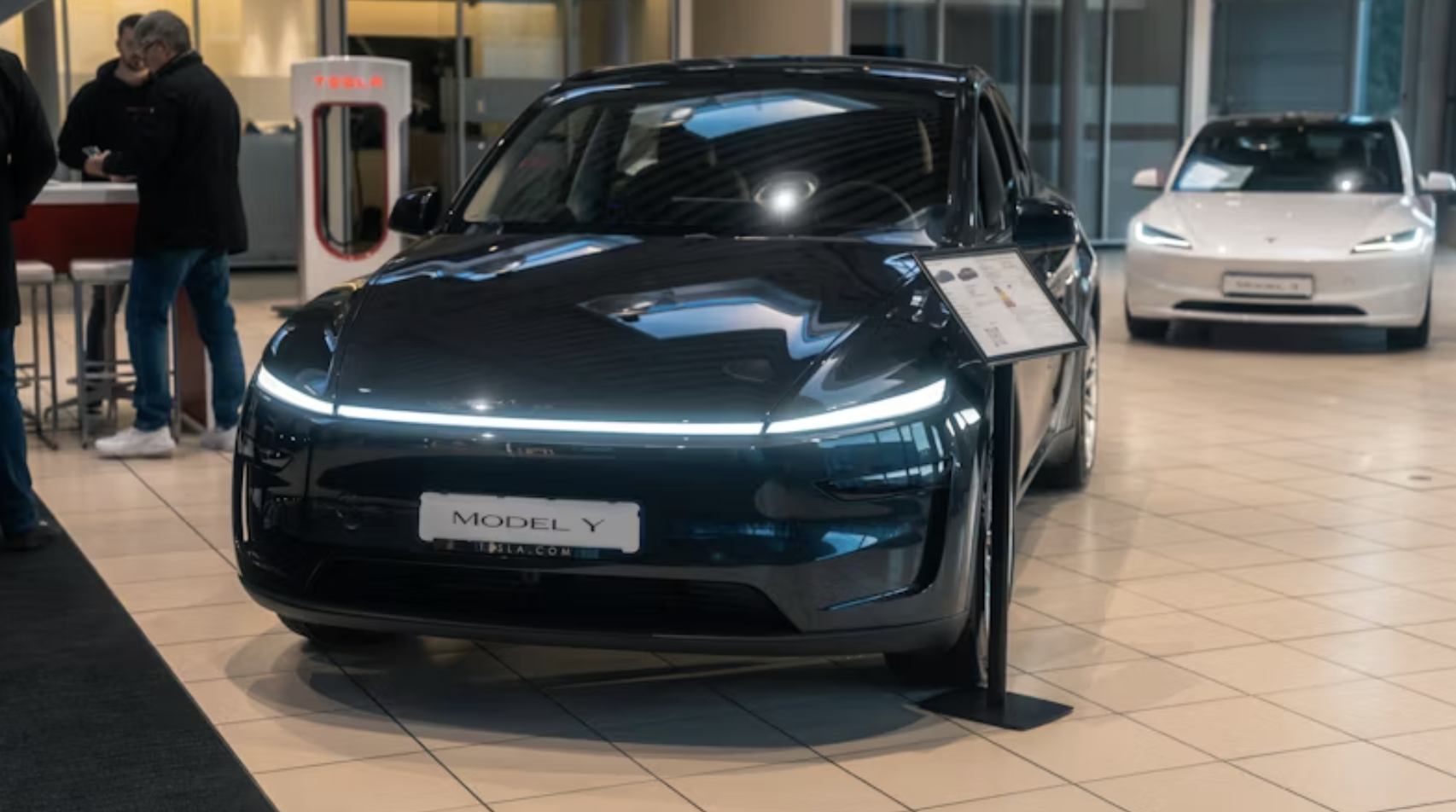 A black Tesla Model Y displayed in the center of a showroom, accompanied by a charging station and an information stand.